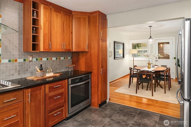 kitchen with brown cabinetry, open shelves, stainless steel appliances, dark countertops, and tasteful backsplash