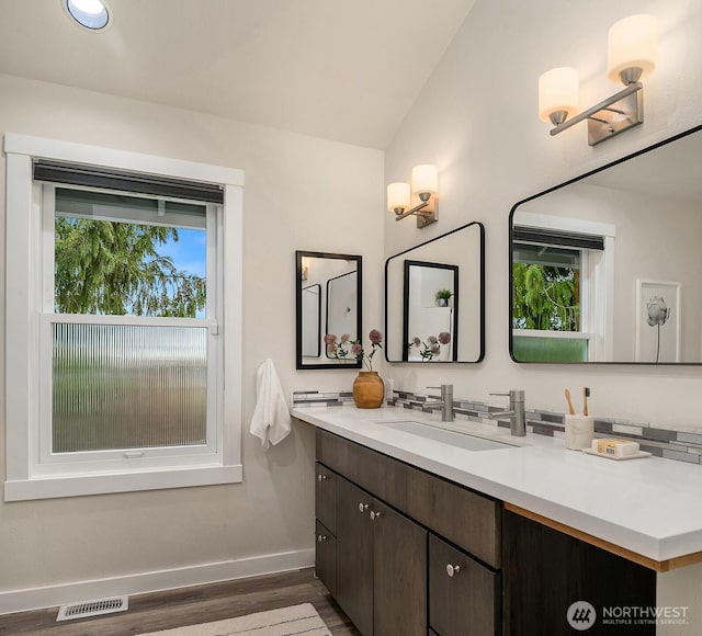 bathroom featuring visible vents, wood finished floors, baseboards, vanity, and vaulted ceiling