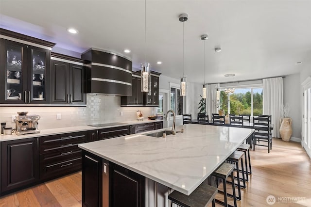 kitchen with black electric stovetop, decorative backsplash, a kitchen breakfast bar, wall chimney exhaust hood, and a sink