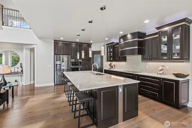 kitchen with backsplash, wall chimney range hood, wood finished floors, stainless steel appliances, and a sink