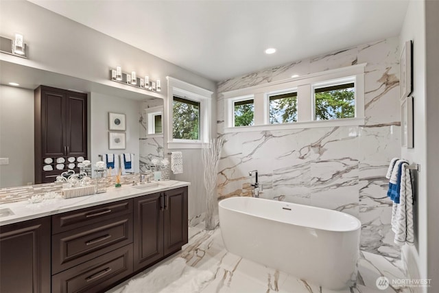 full bathroom featuring a sink, stone wall, a soaking tub, and marble finish floor