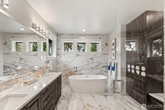 full bathroom with a freestanding tub, marble finish floor, a sink, recessed lighting, and stone wall