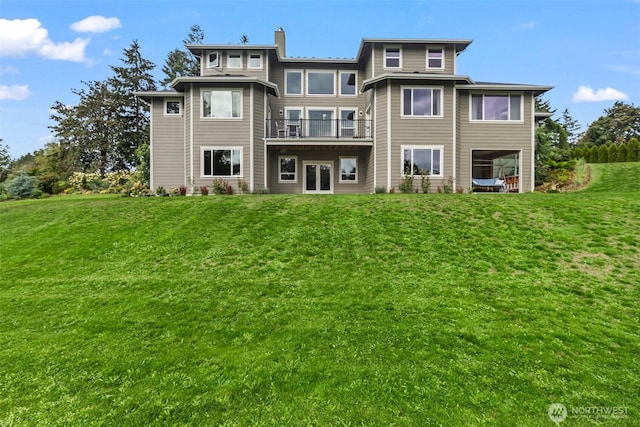 back of house featuring a lawn, a balcony, and a chimney