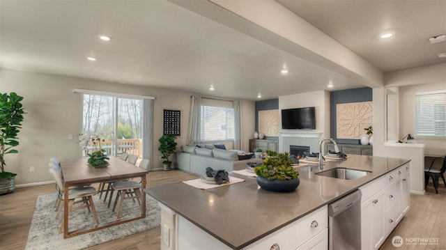 kitchen with a lit fireplace, a sink, light wood-style floors, stainless steel dishwasher, and open floor plan