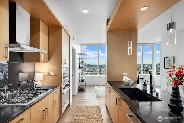 kitchen featuring pendant lighting, a sink, wall chimney range hood, appliances with stainless steel finishes, and light wood finished floors