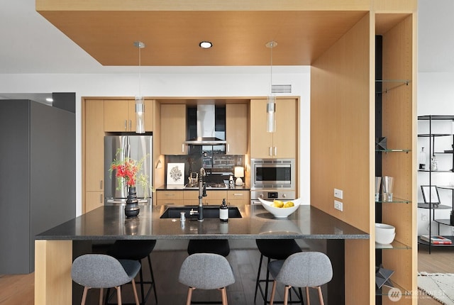 kitchen with a sink, decorative backsplash, stainless steel appliances, a kitchen breakfast bar, and wall chimney exhaust hood