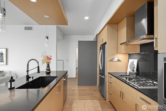 kitchen with visible vents, light brown cabinets, a sink, appliances with stainless steel finishes, and wall chimney range hood