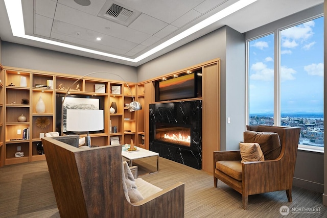 carpeted living area featuring a high end fireplace, visible vents, and a tray ceiling