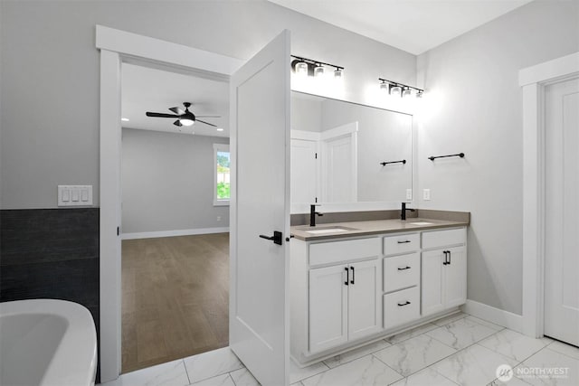 full bathroom featuring marble finish floor, a ceiling fan, a sink, double vanity, and a freestanding bath