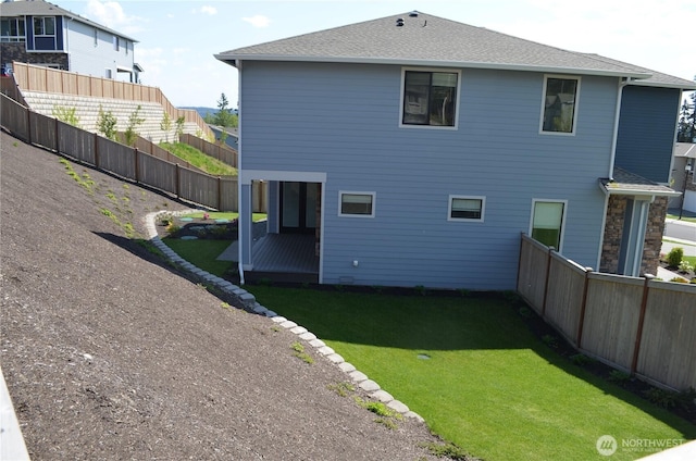 back of house with fence, a shingled roof, and a lawn