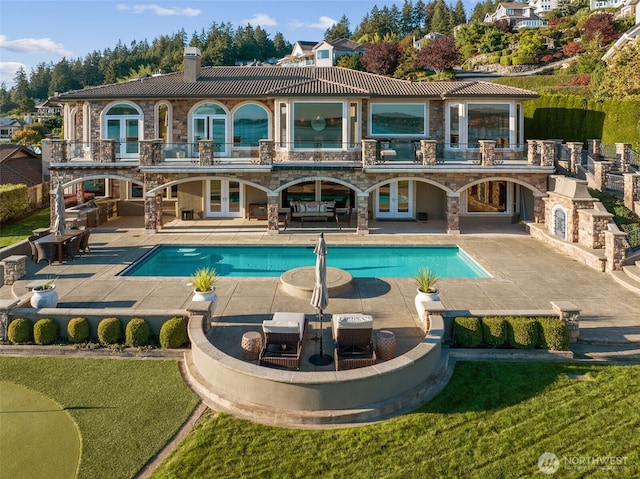 rear view of property with french doors, stone siding, a balcony, and a patio area