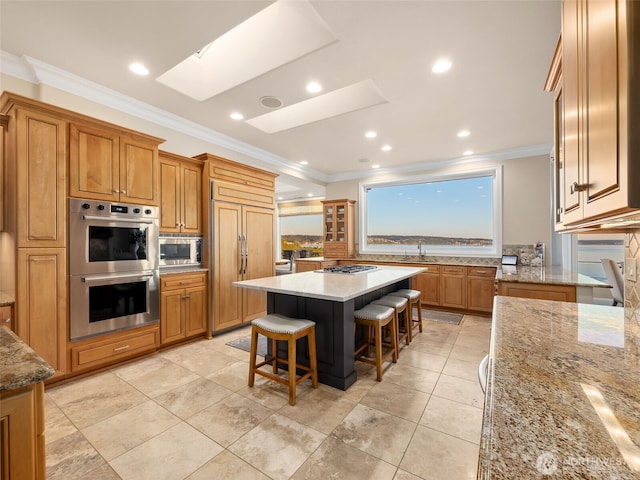 kitchen with crown molding, built in appliances, a kitchen breakfast bar, a skylight, and brown cabinetry