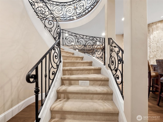 stairs with a high ceiling, baseboards, and wood finished floors