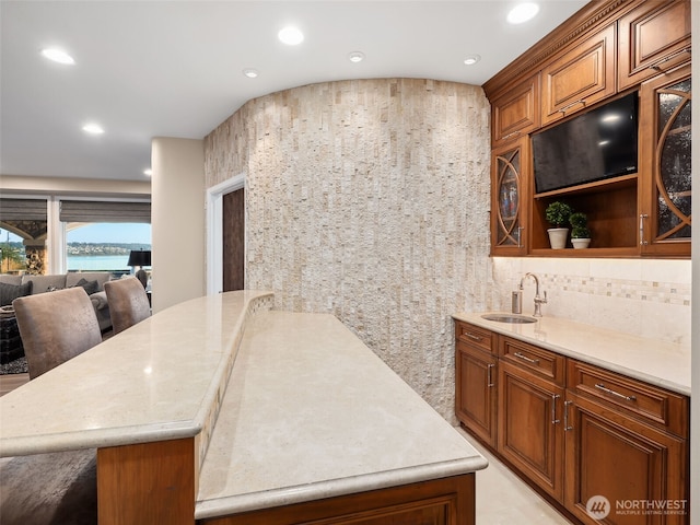 kitchen featuring backsplash, recessed lighting, brown cabinets, a peninsula, and a sink