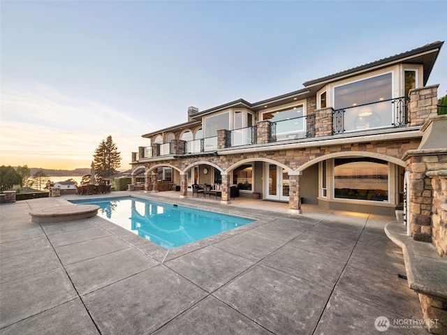 pool at dusk with a patio, french doors, and an outdoor pool