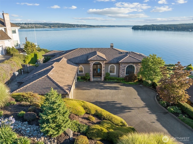 view of front of home with driveway, a chimney, stone siding, a water view, and a tiled roof