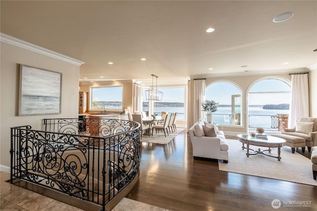 living room featuring wood finished floors, baseboards, recessed lighting, ornamental molding, and a water view