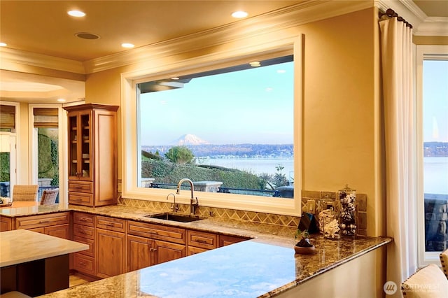 kitchen with light stone counters, ornamental molding, a water view, and a sink