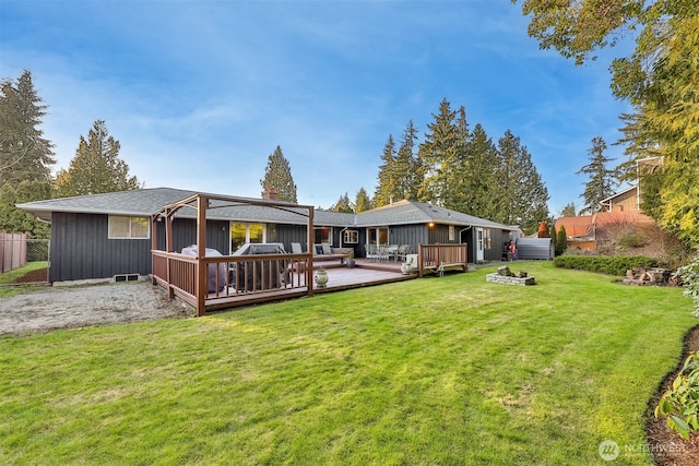 rear view of property featuring a deck, an outdoor fire pit, fence, a yard, and board and batten siding