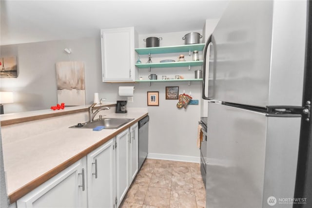 kitchen featuring a sink, appliances with stainless steel finishes, white cabinets, light countertops, and baseboards