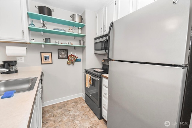 kitchen with stainless steel microwave, freestanding refrigerator, black electric range, white cabinets, and a sink