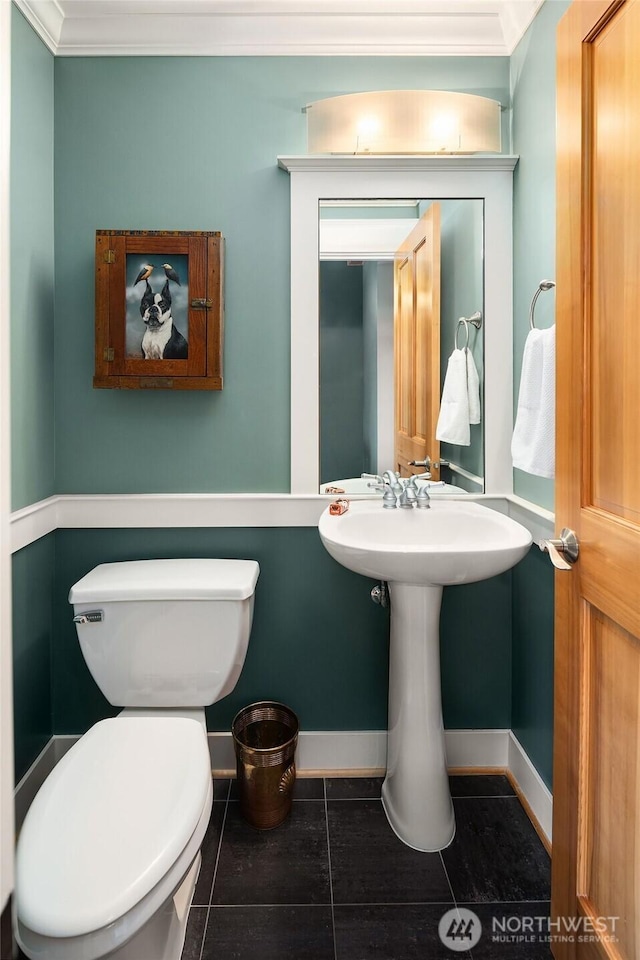 half bath with tile patterned floors, toilet, baseboards, and ornamental molding