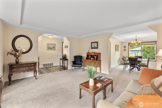 living room with visible vents, a raised ceiling, an inviting chandelier, baseboards, and light colored carpet