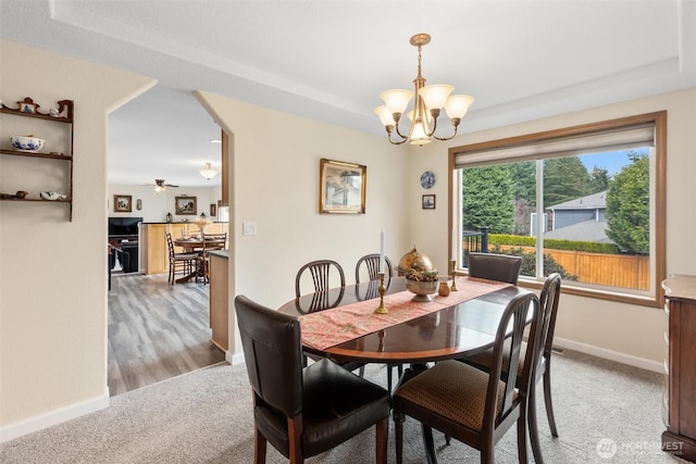 dining space featuring ceiling fan with notable chandelier, carpet flooring, baseboards, and arched walkways