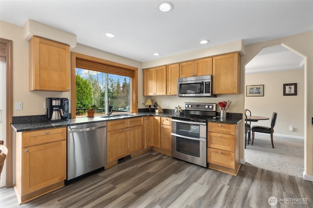 kitchen with dark wood-type flooring, a sink, recessed lighting, arched walkways, and appliances with stainless steel finishes