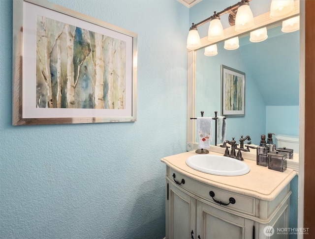 bathroom with a textured wall, vanity, and vaulted ceiling