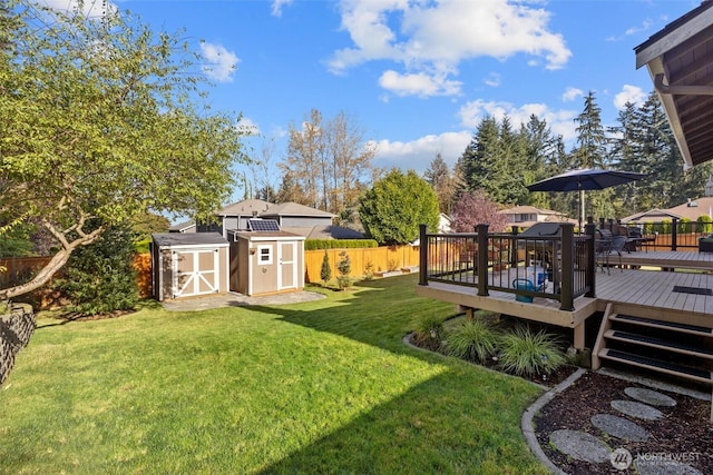 view of yard with an outbuilding, a deck, a storage shed, and a fenced backyard