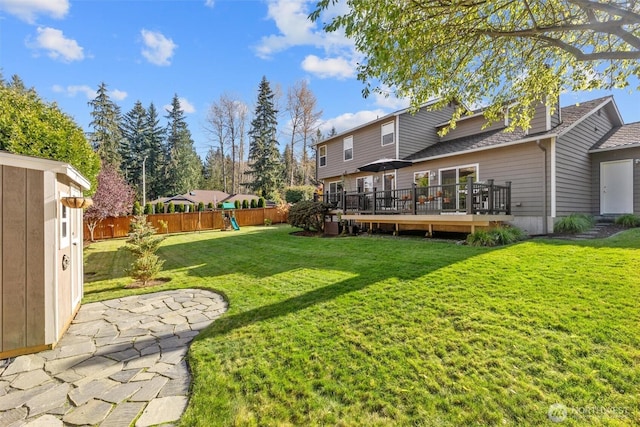 view of yard with a wooden deck, a fenced backyard, and a playground