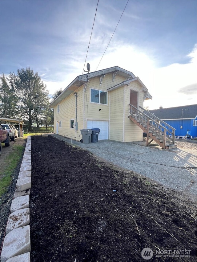 view of side of property featuring stairs, an attached garage, and driveway