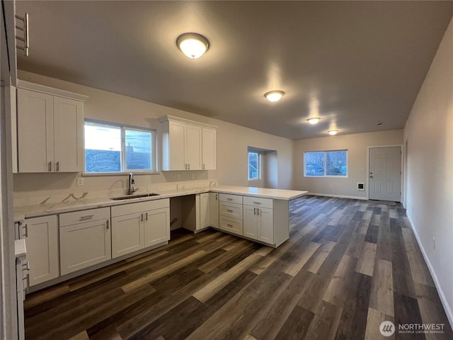 kitchen with baseboards, dark wood finished floors, a peninsula, a sink, and white cabinets