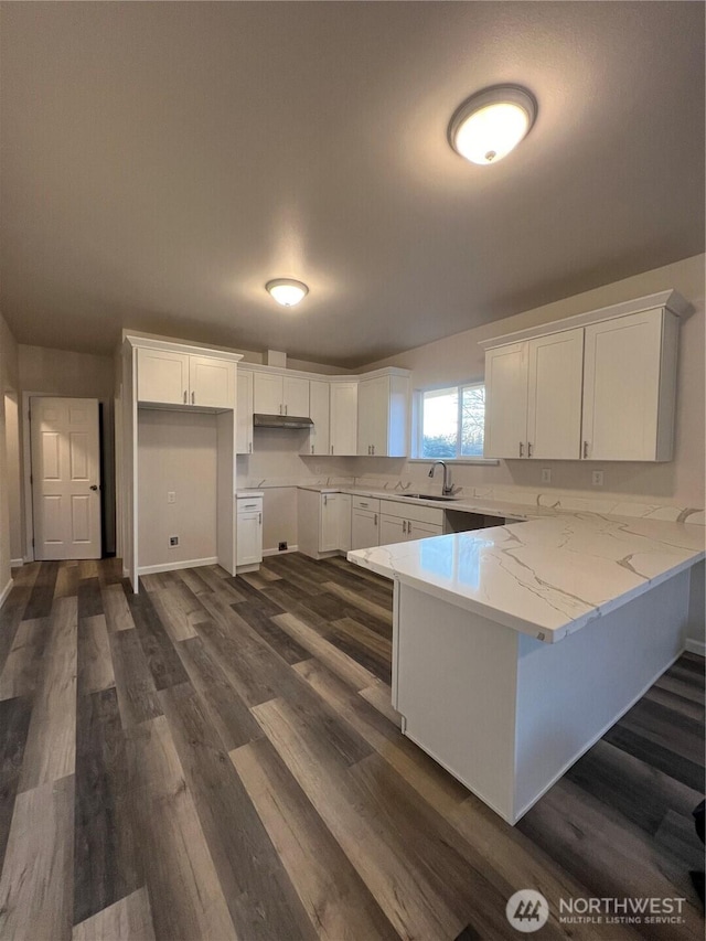 kitchen with dark wood-type flooring, a sink, light stone counters, white cabinetry, and a peninsula