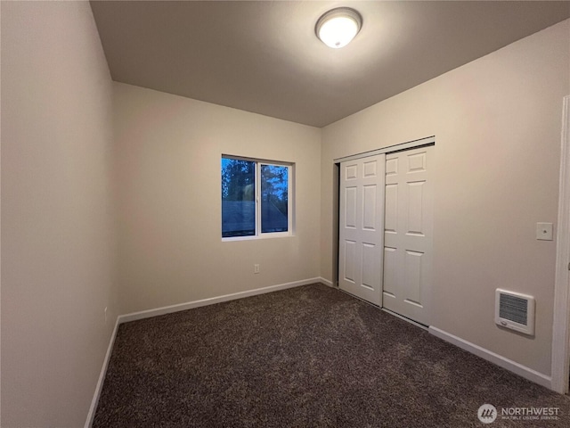 unfurnished bedroom featuring visible vents, dark colored carpet, a closet, and baseboards