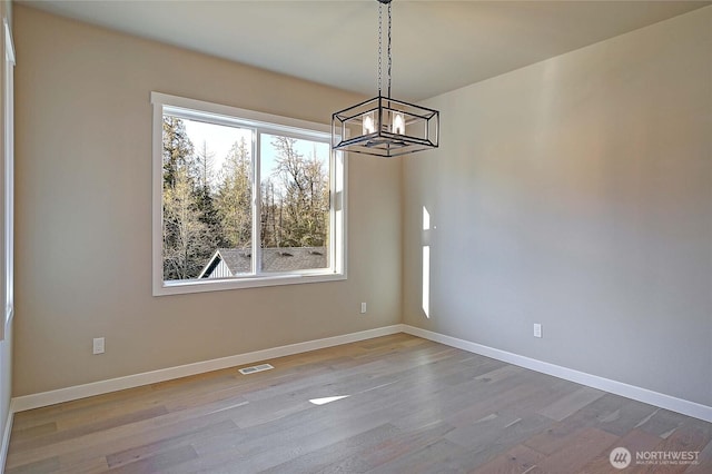 unfurnished dining area with visible vents, baseboards, a notable chandelier, and wood finished floors