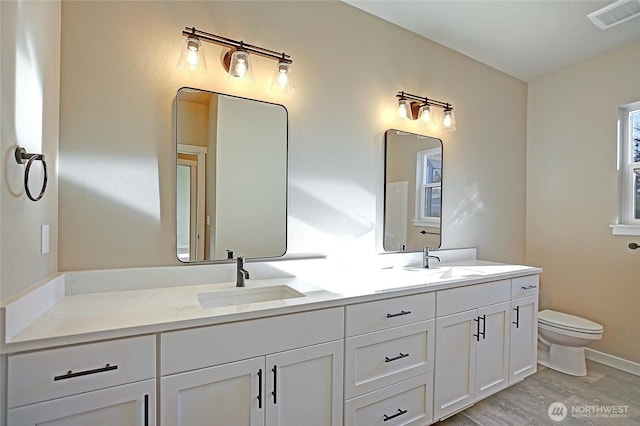 bathroom with double vanity, toilet, visible vents, and a sink