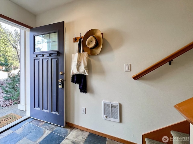 entrance foyer featuring heating unit, stone tile floors, stairs, and baseboards