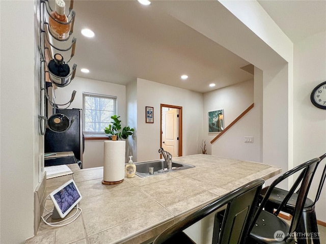 kitchen with tile counters, recessed lighting, refrigerator, and a sink