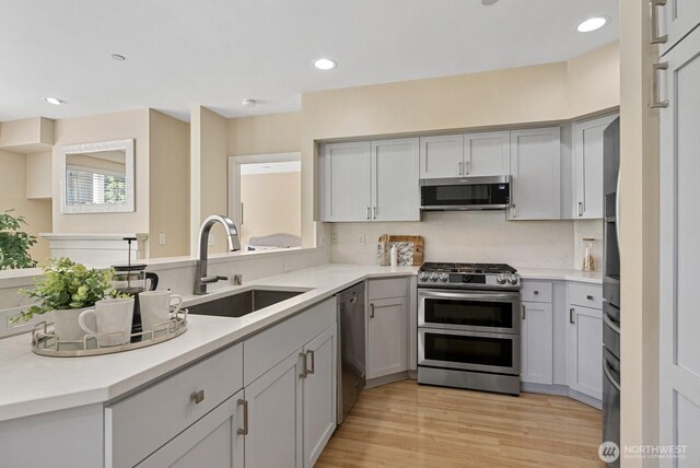 kitchen featuring light wood-type flooring, a sink, recessed lighting, stainless steel appliances, and light countertops