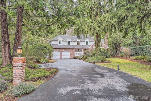 view of front of property with driveway, a front yard, a garage, brick siding, and a chimney