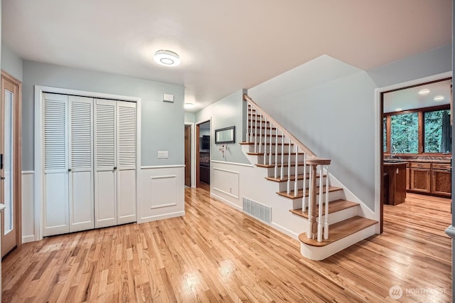 interior space with stairs, visible vents, light wood finished floors, and wainscoting