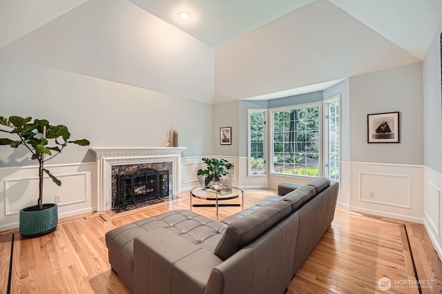 living room featuring light wood-type flooring, a premium fireplace, vaulted ceiling, wainscoting, and a decorative wall