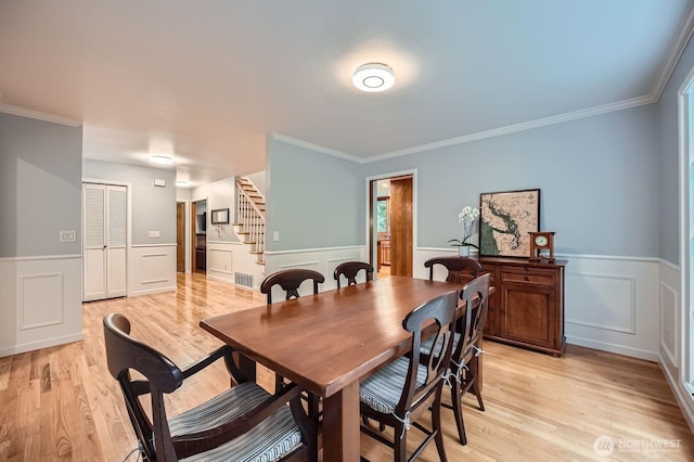 dining space featuring light wood-type flooring, stairway, and a wainscoted wall