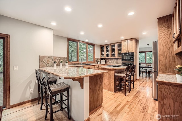 kitchen with a breakfast bar, a sink, black microwave, light wood-type flooring, and backsplash