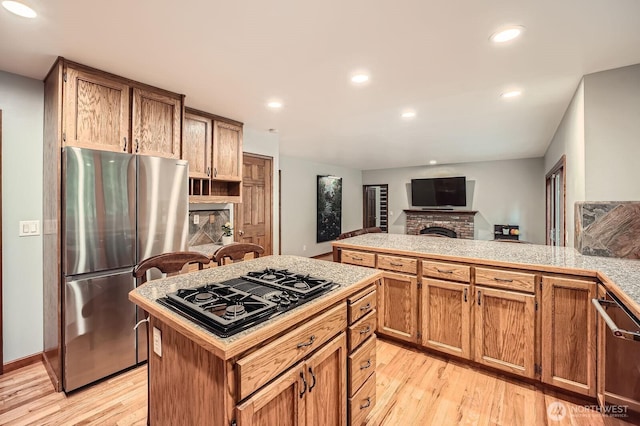 kitchen featuring light wood finished floors, a brick fireplace, black gas cooktop, recessed lighting, and freestanding refrigerator