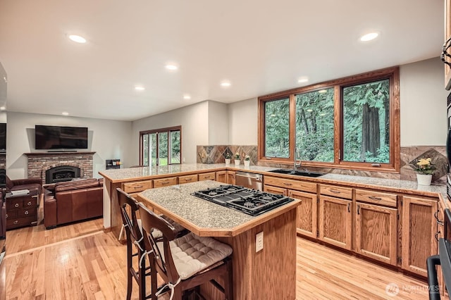 kitchen with light wood-style flooring, black gas stovetop, a sink, a breakfast bar area, and tile counters