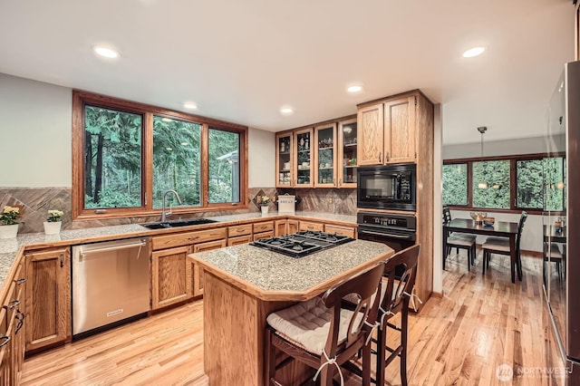 kitchen featuring a breakfast bar area, black appliances, light wood-style flooring, and a sink