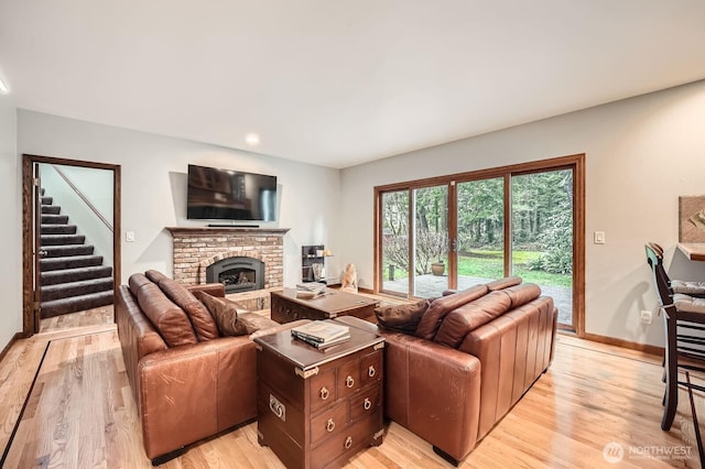 living area with stairway, baseboards, light wood-style floors, and a brick fireplace